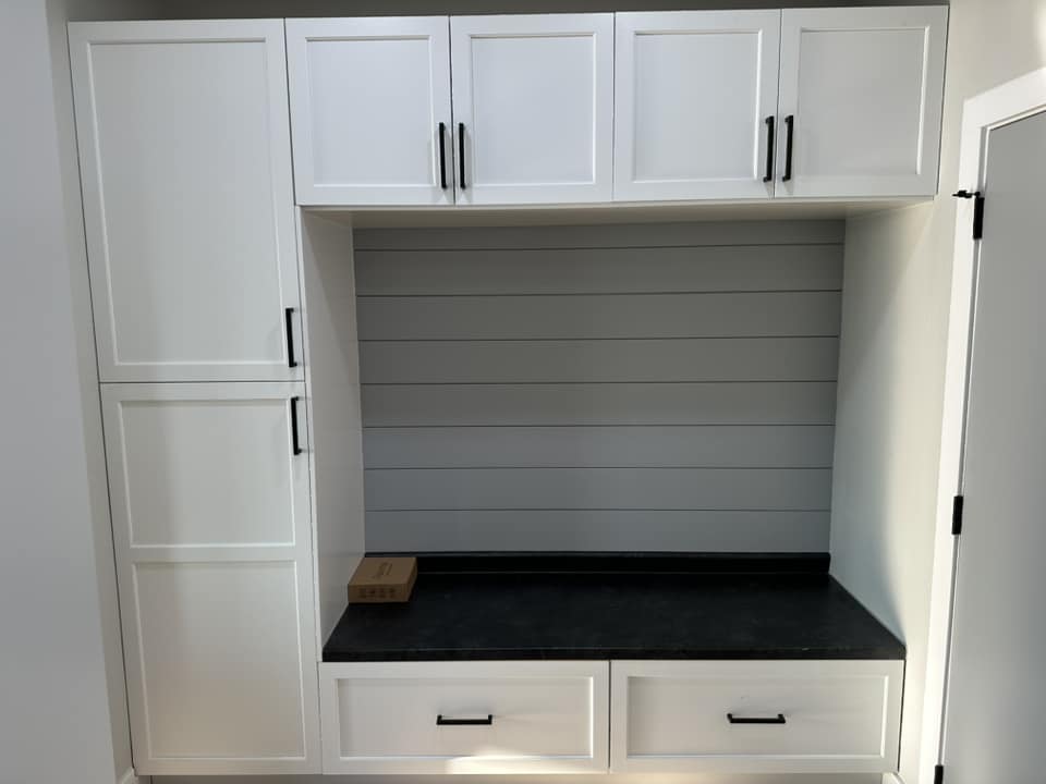 Finished mudroom with white shaker built-in cabinets, black granite bench seat, and shiplap backsplash